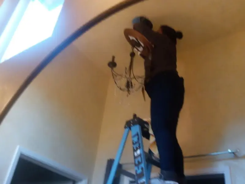 Electrician installing a chandelier in a San Diego Country Estates residence